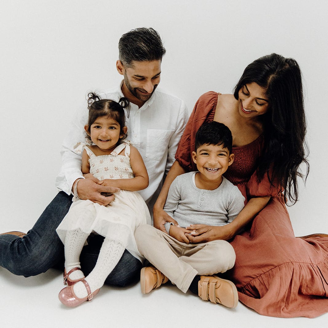 Family of four sitting together on a white background
