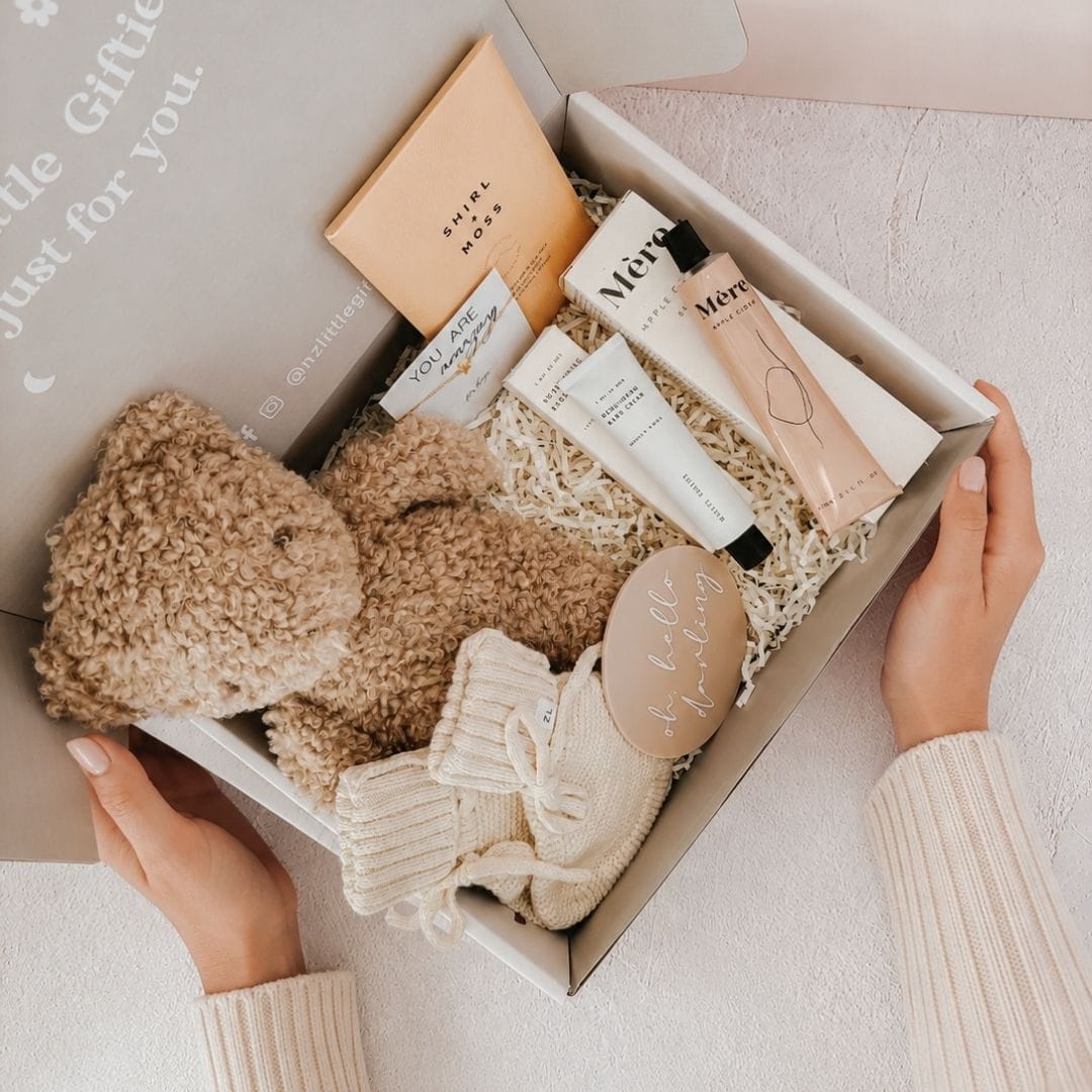 Open gift box filled with baby gifts and self-care products, held by hands